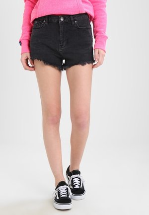 Shorts en denim noir avec ourlet effiloché, taille haute, fermeture à bouton à l'avant et passants de ceinture, associés à des baskets noires basses.