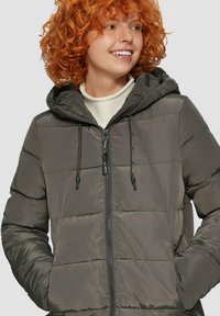 Veste rembourrée grise avec capuche, dotée d'une fermeture éclair à l'avant et de cordons de serrage. Texture lisse avec un piquage horizontal et des poches latérales.