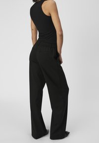 Zwarte geribbelde tanktop gecombineerd met losse zwarte broek met een elastische tailleband en zijzakken, gezien vanaf de achterkant.