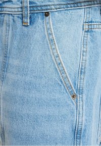 Lyseblå denim shorts med en struktureret overflade, der har en forlommes, orange syninger og en sort knapdetalje på taljen.