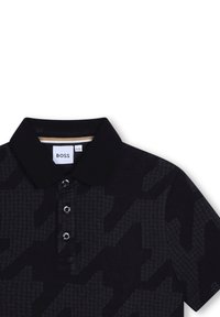Polo noir avec un motif pied-de-poule subtil, trois boutons au col et des accents de col contrastants. Étiquette de marque visible.