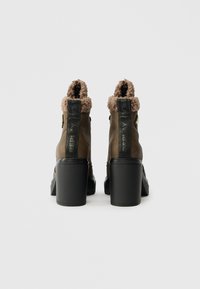 Hnědé kožené kotníkové boty s texturovaným béžovým umělým kožíškem na límci, černým tlustým podpatkem a černou kapsičkou s logem na zadní straně.