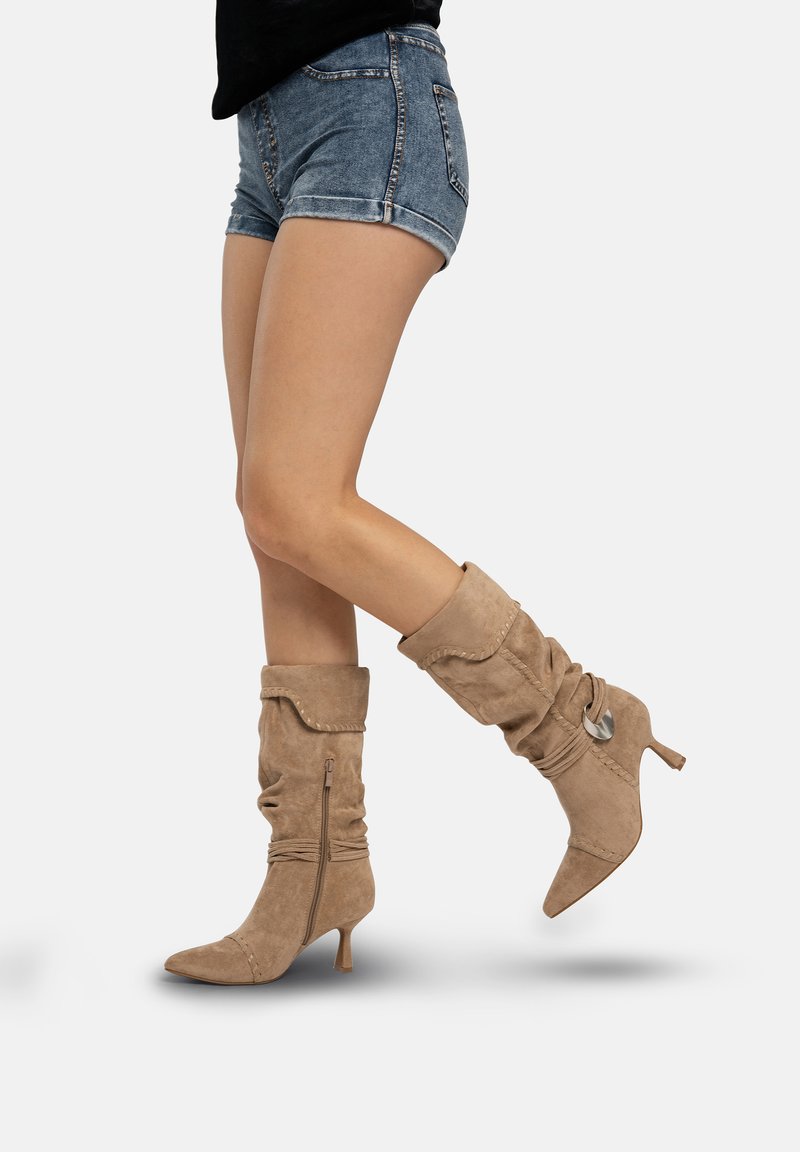 Beige suède slouchlaarzen met een spitse neus en een slanke hak. Voorzien van een ritssluiting en decoratieve stiksels langs de schacht.