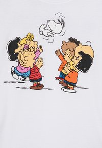 Valkoinen t-paita, jossa on kuusi piirroslasten hahmoa eri väreissä ulottumassa ylös; heidän yllään lentää piirroskoira Snoopy.