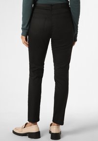 Schwarze, figurbetonte Hosen aus glattem Stoff mit einem hohen Bund, Taschen und einem zulaufenden Bein-Design. Kombiniert mit beigen Slippern.