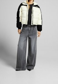 Czarna i biała kurtka puchowa o skróconym kroju; szare szerokie spodnie z wyblakłą teksturą; oba elementy charakteryzują się swobodnymi, luźnymi sylwetkami.