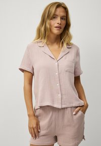Lichtroze pyjamastel met korte mouwen van zacht, gestructureerd stof. Knopsluiting bovenstuk met een zak en bijpassende shorts met een elastische tailleband.