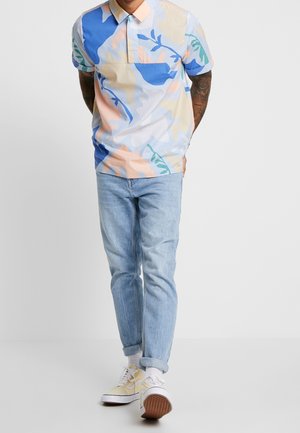 Multicolored short-sleeve polo shirt with a mix of blue, peach, and beige patterns; paired with light wash jeans and yellow sneakers.