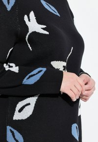 Gestickter Pullover in Schwarz mit weißen und blauen Blumenmustern. Verfügt über einen runden Halsausschnitt und lange Ärmel mit gerippten Abschlüssen. Weiche Textur.