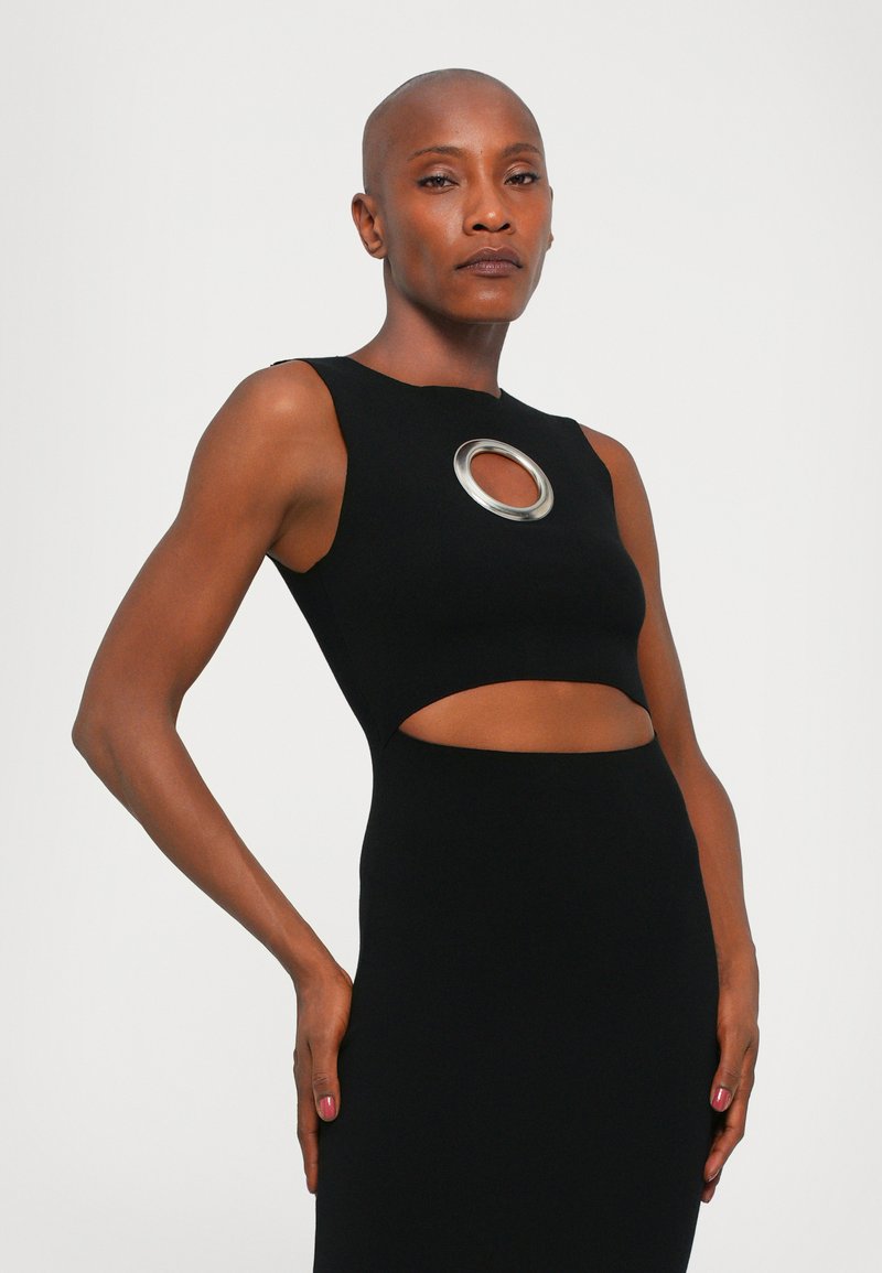 Black sleeveless top with a circular silver accent at the neckline and cut-out details, made from a fitted stretch fabric.