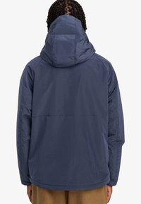 Granatowa kurtka z kapturem wykonana z teksturowanej tkaniny, o prostym kroju i lekkim, oddychającym materiale, zaprojektowana do aktywności na świeżym powietrzu.