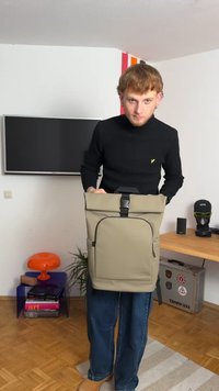 Rucsac bej cu vârf rulant, fabricat dintr-un material durabil, dotat cu un buzunar frontal cu fermoar, bretele ajustabile și închidere cu capse.