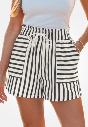 Donna che indossa pantaloncini a righe bianche e nere a vita alta con coulisse bianca e grandi tasche frontali, abbinati a un top bianco senza maniche.