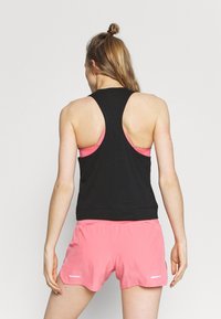 Top atletico senza maniche di colore nero con schiena arrotondata, abbinato a pantaloni corti rosa. Presenta un design a tinta unita e una vestibilità comoda.