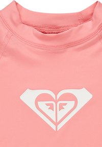 Räven punainen rash guard korkealla kauluksella, jossa on valkoinen sydämen muotoinen logo, jossa on nuoliakenteita keskellä. Sujuva, joustava kangas.