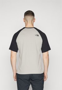 Camiseta de manga corta para hombre con cuerpo gris claro y mangas raglán negras. Presenta un pequeño logo en la parte posterior. Material de algodón.