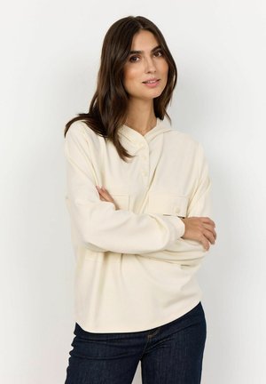 Crème, sweatshirt met capuchon en knoopsluiting, voorzien van twee voorzakken; zachte stof, ontspannen pasvorm, gecombineerd met donkere jeans.