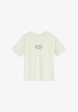 Jasna kremowa koszulka z krótkim rękawem i okrągłym dekoltem. Na koszulce w czarnym kolorze nadrukowany tekst "DIVERSE HERITAGE Original". Prosty design.