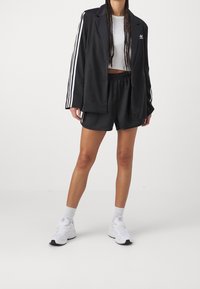 Černý oversize blejzr s bílými proužky na rukávech, bílý krátký top, černé šortky a bílé tenisky s černými detaily.