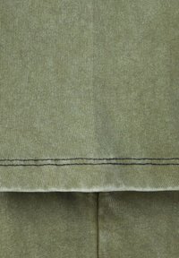 Olijfgroen stof close-up, ribbelstructuur; contrasterende donkere stiksels langs de zoom; gladde afwerking met een zachte uitstraling.