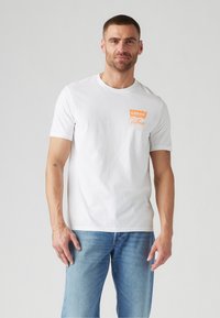 Bijela pamučna majica s malim narančastim Levi's logotipom i natpisom "California". Standardni kroj, kratki rukavi, u kombinaciji s trapericama.