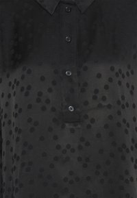 Black shirt with a collared design, featuring subtle textured polka dots, front buttons, and a smooth fabric finish.