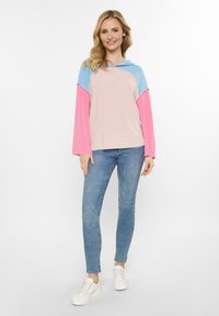 Farbblockierter Hoodie aus hellblauem, rosa und beigem Rippstoff. Verfügt über eine Kapuze, lange Ärmel und eine lockere Passform. Kombiniert mit blauen Jeans und weißen Sneakers.