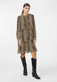 Abito a fantasia leopardata con maniche lunghe e orlo a volant. Realizzato in tessuto leggero. Indossato con stivali neri al ginocchio e dettaglio con zip.