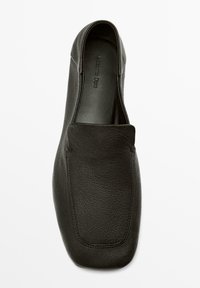 Scarpa slip-on in pelle nera con una texture liscia, punta arrotondata e dettagli di cuciture sottili. La soletta è brandizzata.