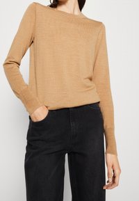 Lichtbruine, lange mouwen trui van een zachte gebreide stof met een ronde hals. Gepaard met zwarte, hoge taille, wijde broek.