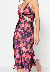 Satin klänning med ett flerfärgat blommönster i rosa, lila och grönt; designad med en snurrad front och utklippta sidor.