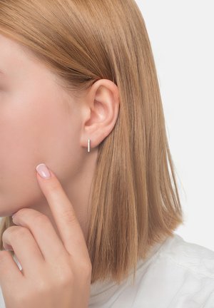 Silberne Creolen, die an einem Modell präsentiert werden. Glattes, minimalistisches Design mit einer polierten Oberfläche, das die kurzen, glatten Haare des Modells ergänzt.