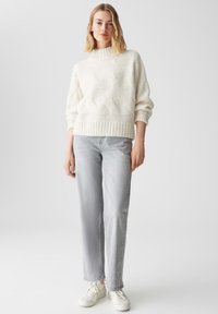 Maglione bianco chunky a collo alto con motivo testurizzato; abbinato a jeans dritti grigi chiari e sneakers bianche.