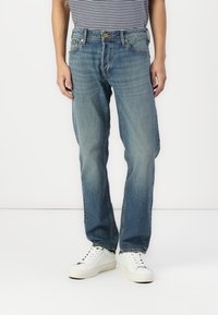 Bleke blauwe denim jeans met een relaxte pasvorm, voorzien van een voorknofsluiting, vijf zakken en een lichte vervaging. G gedragen met witte sneakers.