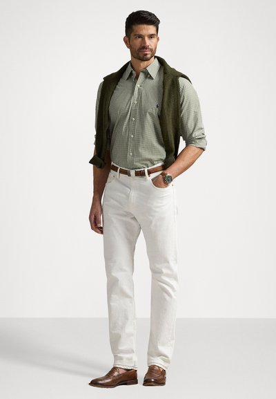 Πράσινο καρό πουκάμισο, ελαιόχρωμο πουλόβερ ριγμένο στους ώμους, λευκά tapered παντελόνια, καφέ δερμάτινα παπούτσια, ρολόι στον καρπό.