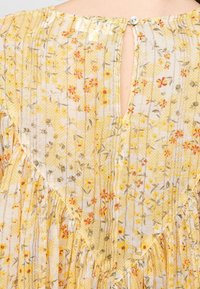 Abito floreale con un tessuto a fantasia giallo e bianco, delicati volant sullo scollo e chiusura con bottoni sul retro.