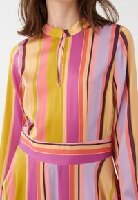 Farbenfrohes Kleid mit vertikalen Streifen in verschiedenen Schattierungen von Pink, Lila und Gelb. Weicher Stoff mit einem Schlüsselloch-Ausschnitt und langen Ärmeln.