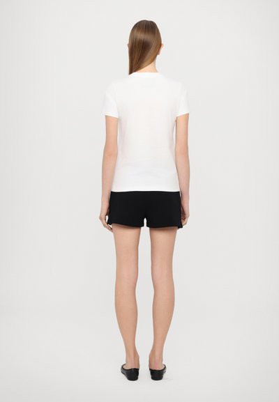 Camiseta blanca de manga corta, de corte estándar, combinada con pantalones cortos negros. La tela parece suave con un diseño simple y sin patrones visibles.