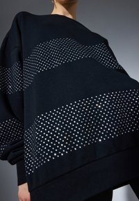 Svart oversized sweatshirt med glittrande silverdetaljer i ett vågmönster, som har en mjuk textur och löst sittande ärmar.