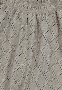 Lichtgrijze textuurstof met een ruitenpatroon en een smocktailleband. Heeft verhoogde stiksels en een subtiele glans.