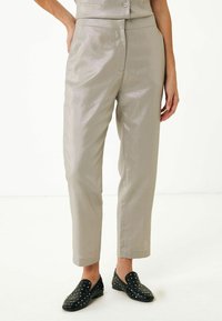 Ljusgrå tygbyxor med en subtil lyster, tapered passform, sidofickor och flat front; matchade med svarta, prickiga slip-on skor.