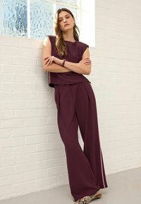 Burgundy matching set featuring a sleeveless top and wide-leg trousers with side stripes. Smooth fabric with a relaxed fit, minimalist design.