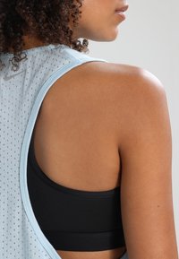 Canottiera atletica azzurro chiaro in tessuto perforato, abbinata a un reggiseno sportivo nero. Presenta un collo rotondo e un design con schiena scoperta.