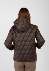 Giacca a vento marrone trapuntata con cappuccio, caratterizzata da una finitura lucida e motivi testurizzati in rilievo. Il design è pensato per offrire calore e comfort.