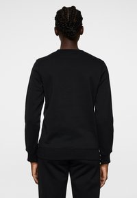 Svart tröja i slät tyg, med rund halsringning och långa ärmar. Ribbad mudd och nederkant. Enkelt design utan synliga logotyper.