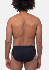 Zwart gestreepte zwemslip gemaakt van een rekbare stof, met een middelhoge tailleband en een gladde textuur, gezien vanuit de achterkant.