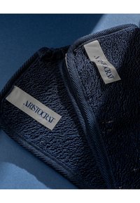 Ręcznik z teksturowanej tkaniny w granatowym kolorze z wyraźnym wzorem tkanym. Etykiety w jasnym kolorze z napisem "ARISTOCRAT" w ciemnych literach.