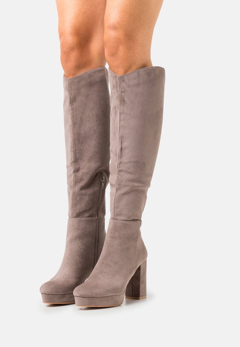 Bottes hautes en suède taupe avec semelles compensées et talons carrés portées sur jambes nues, vues de face et de profil.