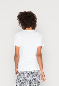 Camiseta de algodón blanca con mangas cortas y cuello redondo. Presenta un diseño de costura tipo raglán. Se lleva con una falda fluida y estampada.