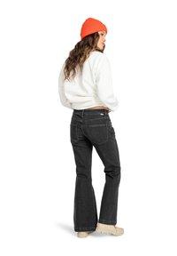 Black flared jeans with two back pockets, paired with a white sweatshirt and orange knit beanie, worn with beige platform shoes.